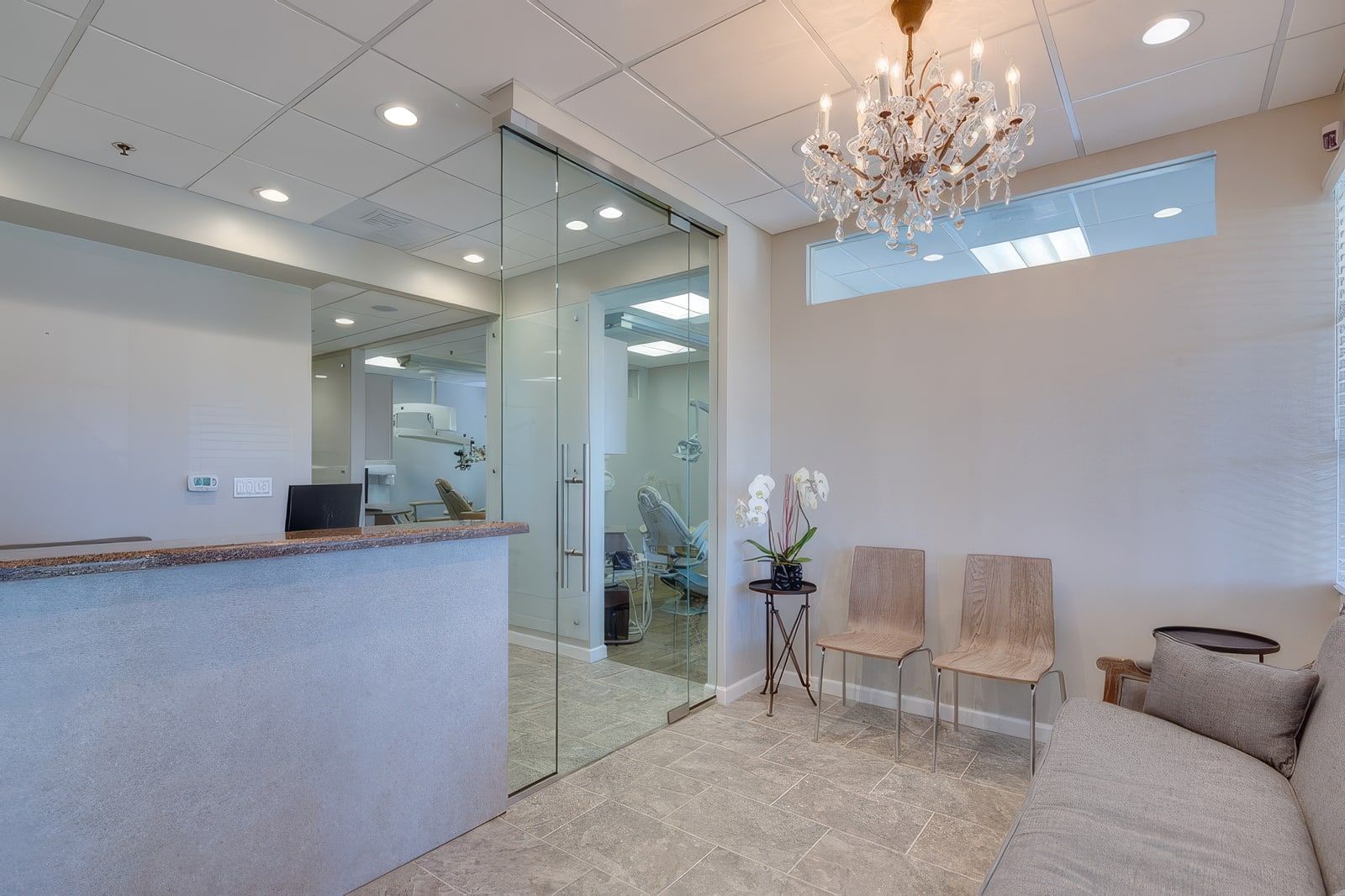 The reception room at Endodontics DDS: a chandelier, a gray sofa, and a glass door to the treatment rooms